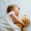 Little baby sleeping on bed embracing soft toy, free space